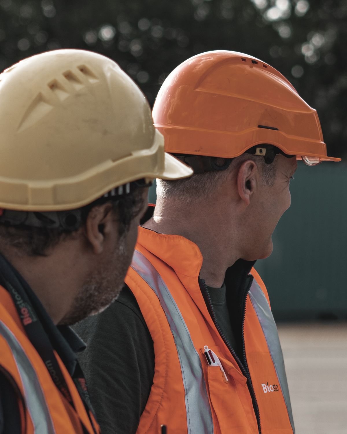Two workers wearing hard hats and orange high-visibility jackets